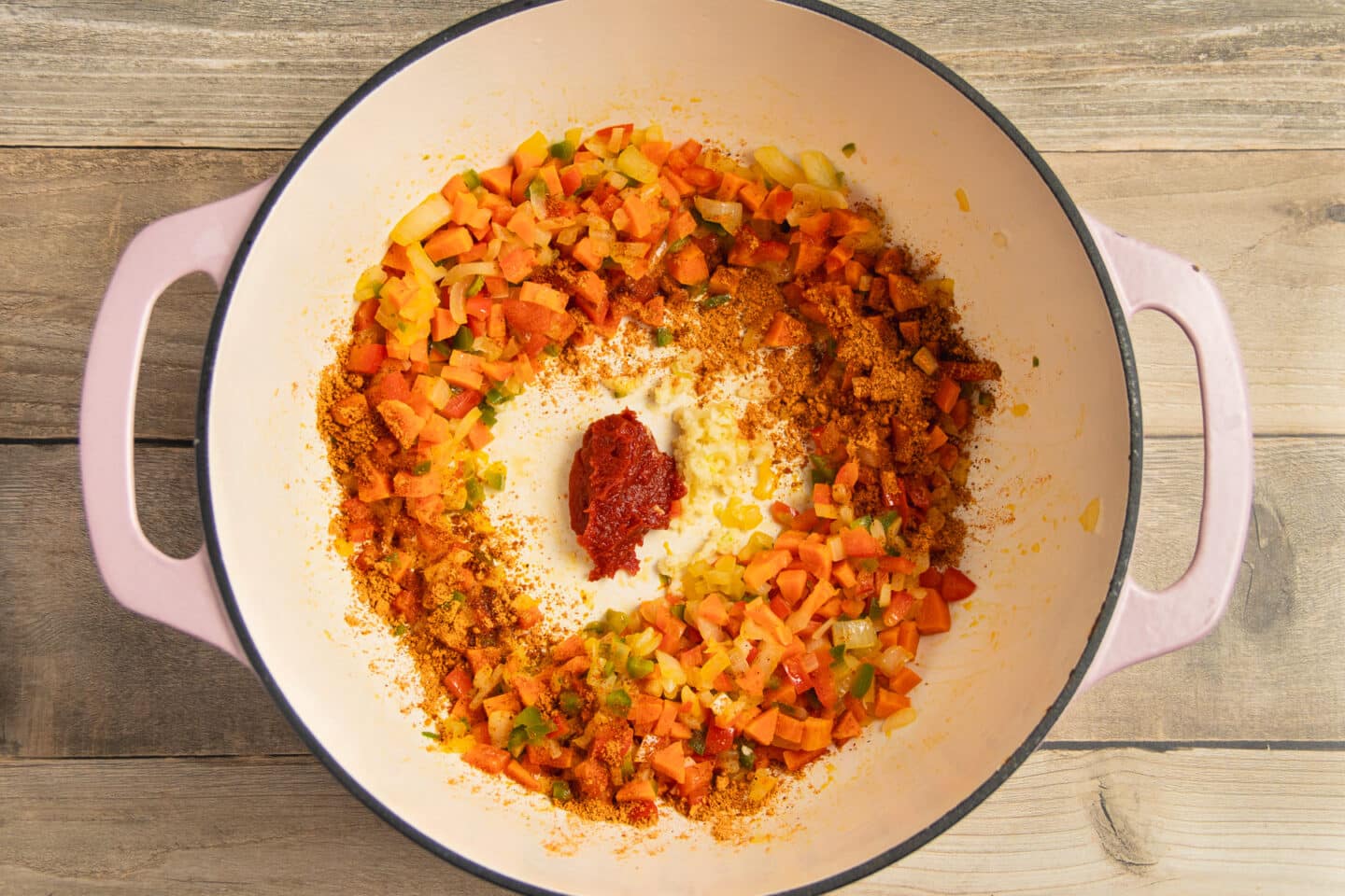 This is a picture of a pot with veggies cooking and added garlic and tomato paste.