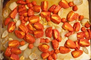 This is a picture of tomatoes, onions and garlic on a baking sheet after roasting.