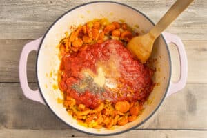 This is a picture of a pot with the veggies and crushed tomatoes added and seasoning added.