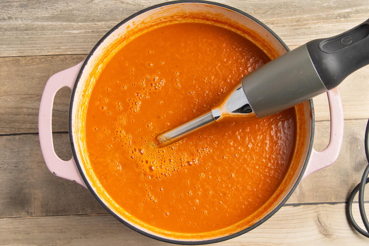 This is a picture of a pot with the soup being blended with an hand immersion blender.