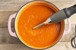 This is a picture of a pot with the soup being blended with an hand immersion blender.