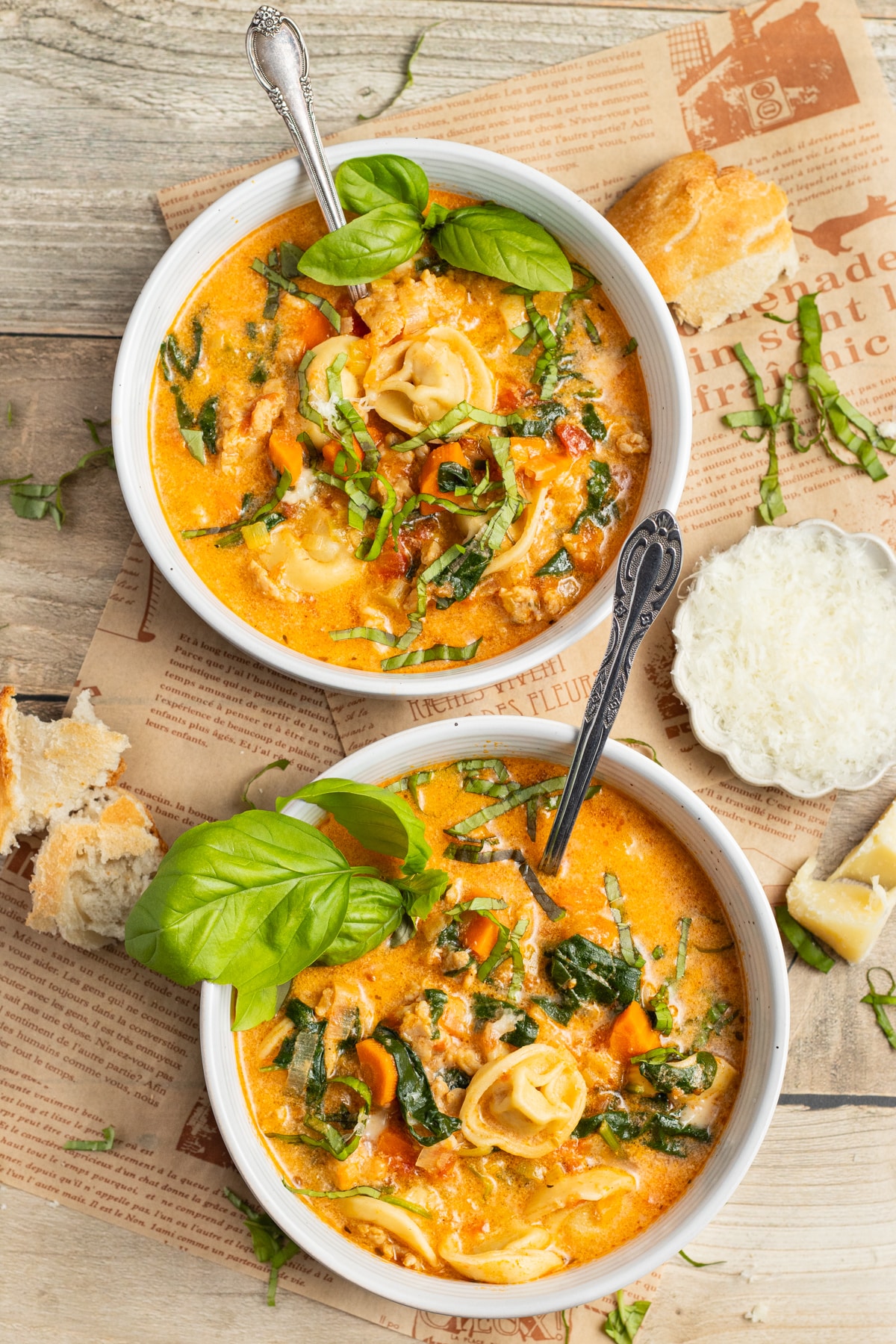 This is a picture of two bowls of tortellini soup with spinach and sausage.