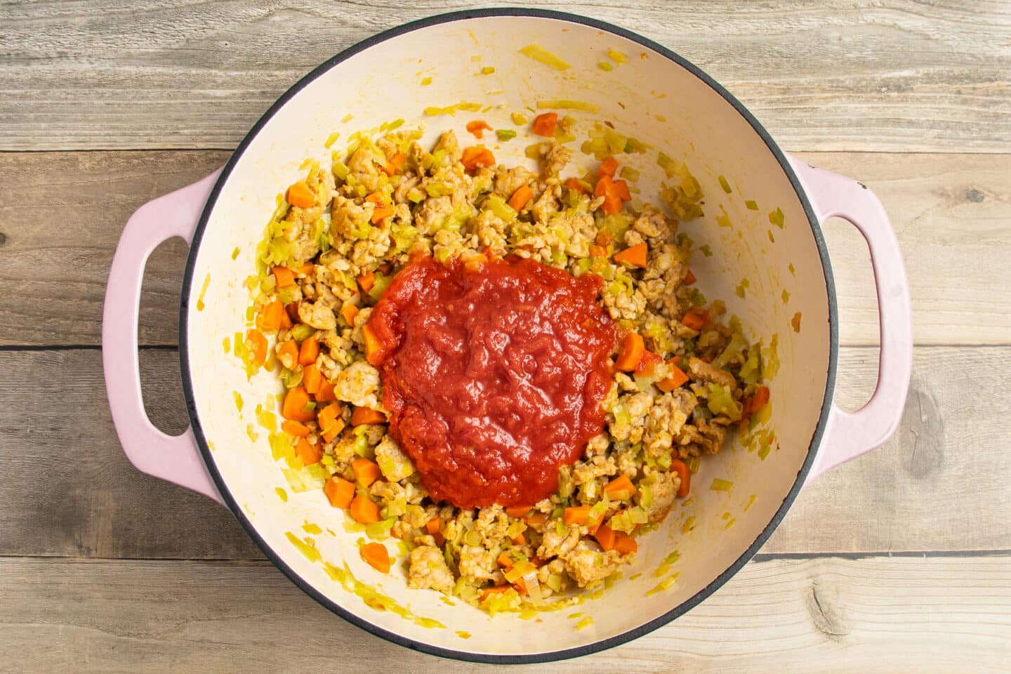 This is a picture of the pot with crushed tomatoes added to the carrots, sausage and leeks.
